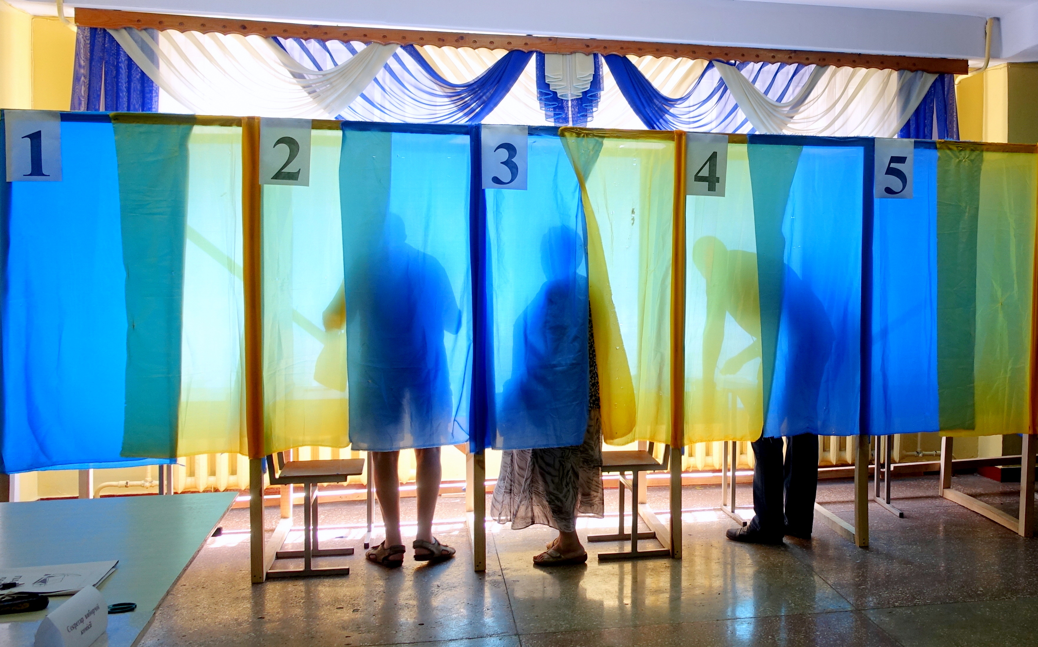 Voters stand behind blue and yellow curtains in poll booths.