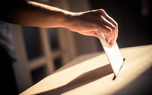 Hand places ballot in ballot box.