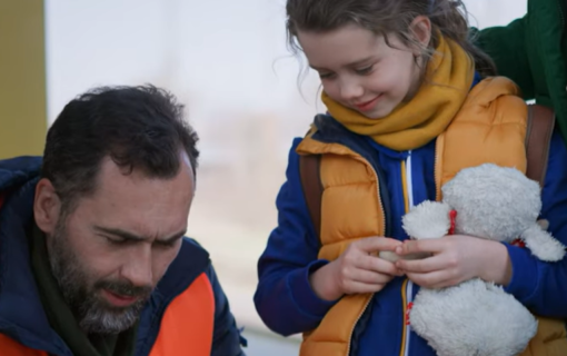 Screenshot from about IFES Ukraine video. Man holding clipboard with young girl holding stuffed animal.