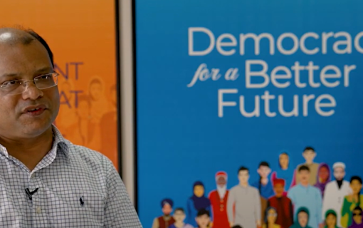 Capture from video. Person speaks in front of boards with IFES vision and mission.