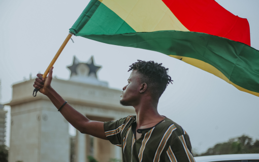 Young man waves Ghanian flag with building in the back on a city street.