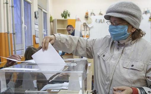 A person wearing a mask puts a ballot into a ballot box.