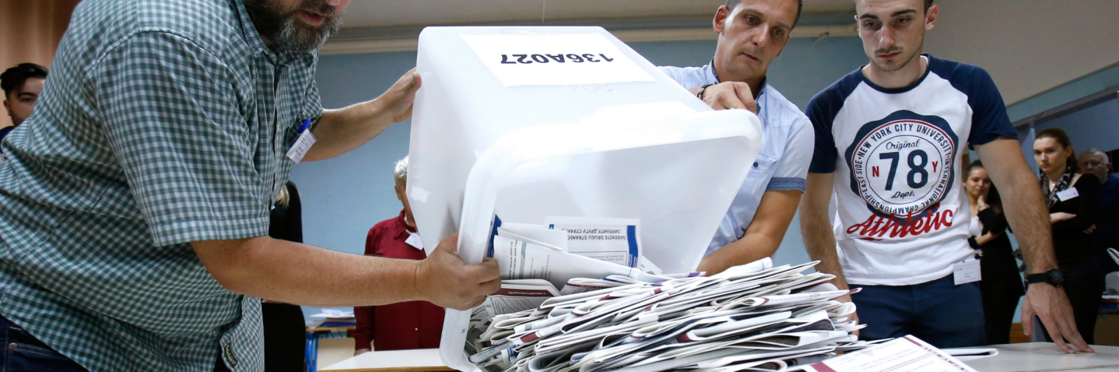 Three Bosnian election workers empty paper ballots from a container onto a table.