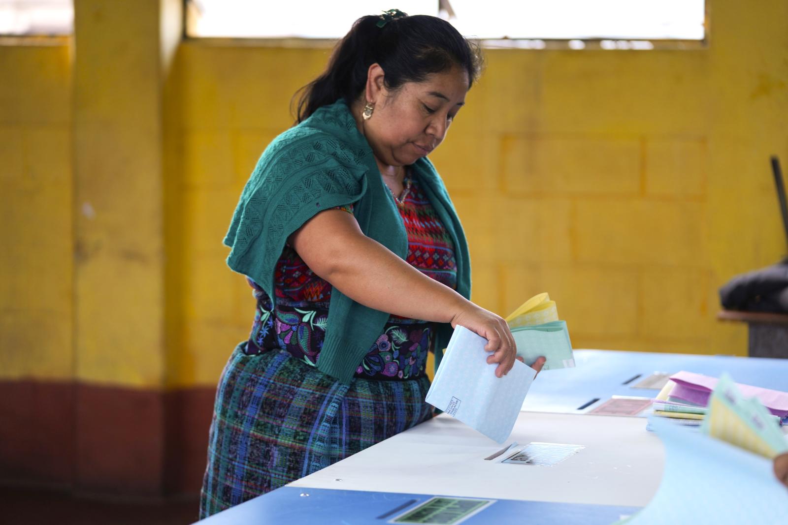 A woman casts her vote into a ballot box.