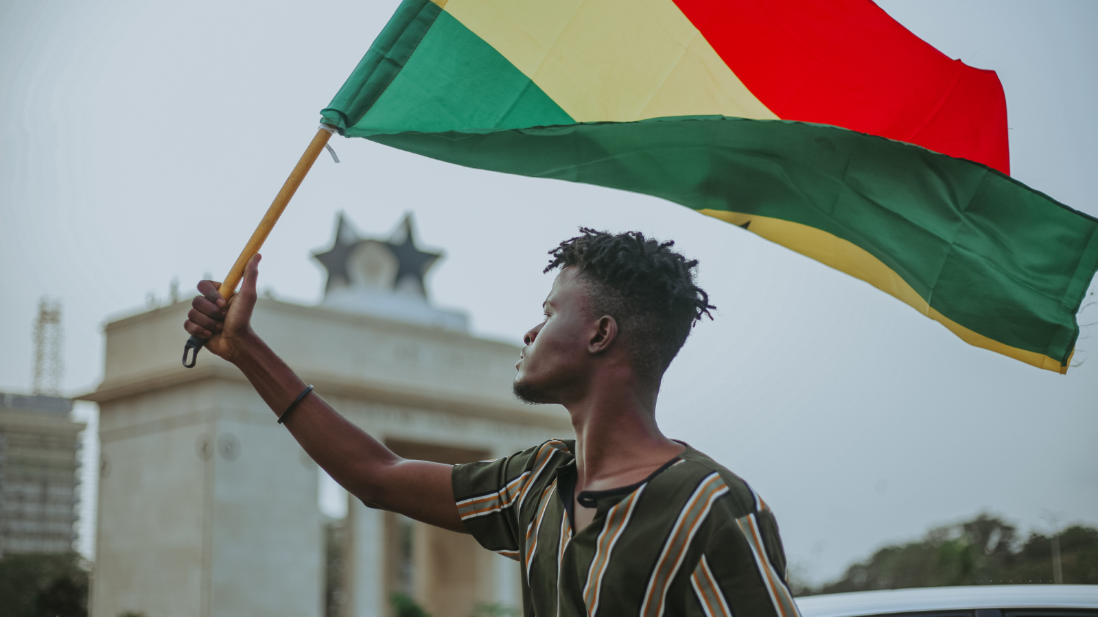 Young man stands on city street in Ghana with Ghanian flag