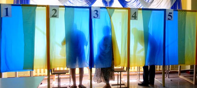 Voters stand behind blue and yellow curtains in poll booths.