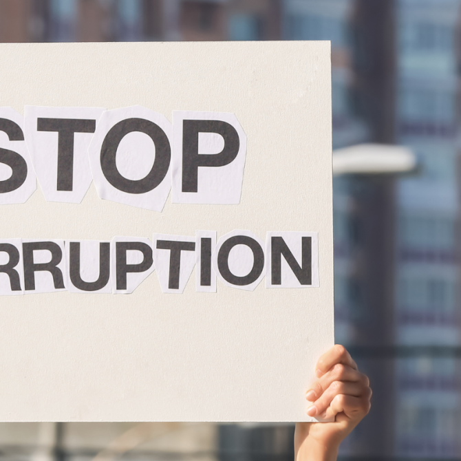 Person on city street holds sign that says stop corruption.