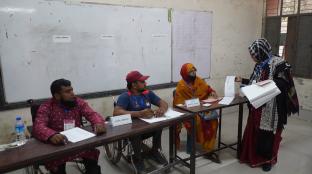Mock polling station set up with poll workers and voters and whiteboard in the background