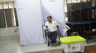 Person using wheel chair returns returns from mock vote with ballot box in the foreground