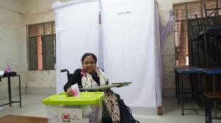 Person using wheel chair places their mock ballot in ballot box