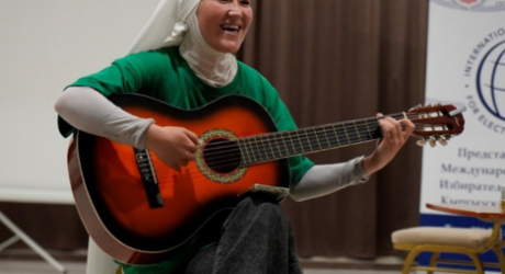 young woman plays guitar while wearing a white hijab and green shirt