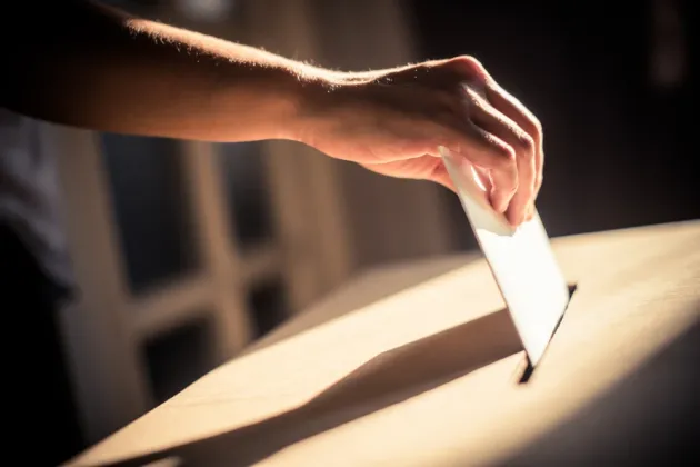 Hand places ballot in ballot box.