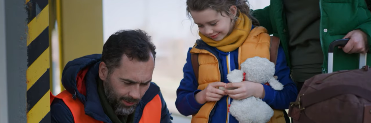 Screenshot from about IFES Ukraine video. Man holding clipboard with young girl holding stuffed animal. 