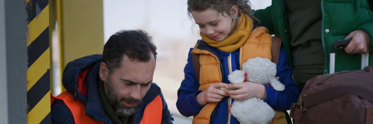 Screenshot from about IFES Ukraine video. Man holding clipboard with young girl holding stuffed animal.