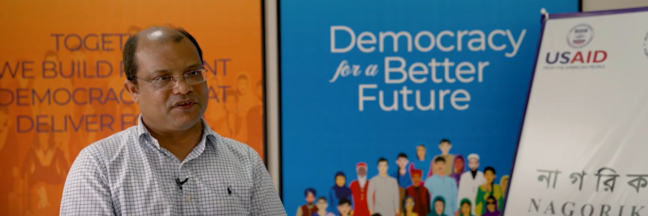 Capture from video. Person speaks in front of boards with IFES vision and mission. 