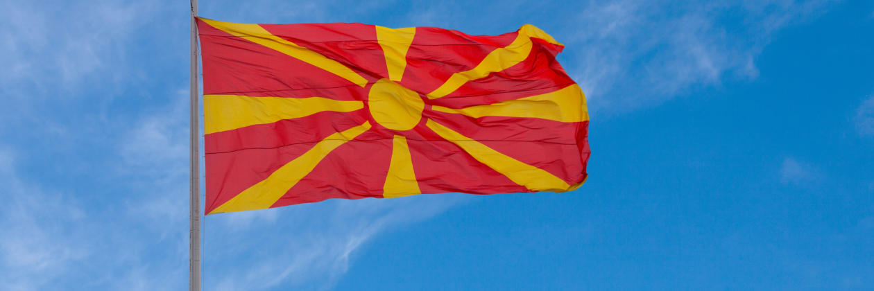 Flag of North Macedonia flying in blue sky.