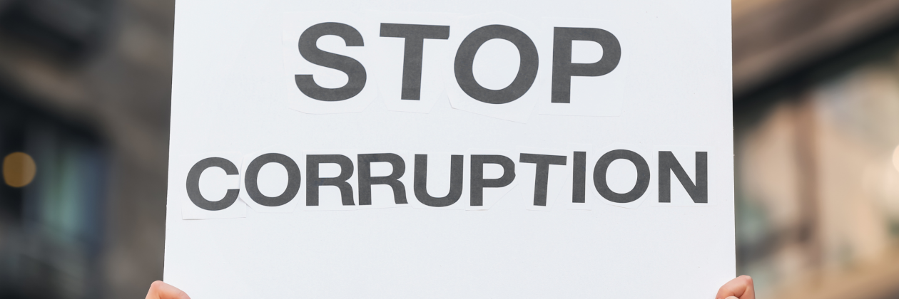 woman holding placard that says stop corruption outdoors. photo credit pixelshot