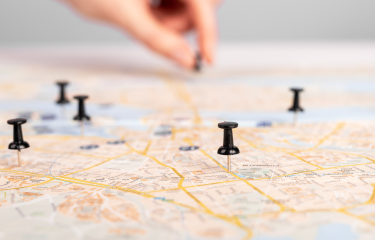 Roadmap with pushpins spread out. Hand in the background with additional pushpin.
