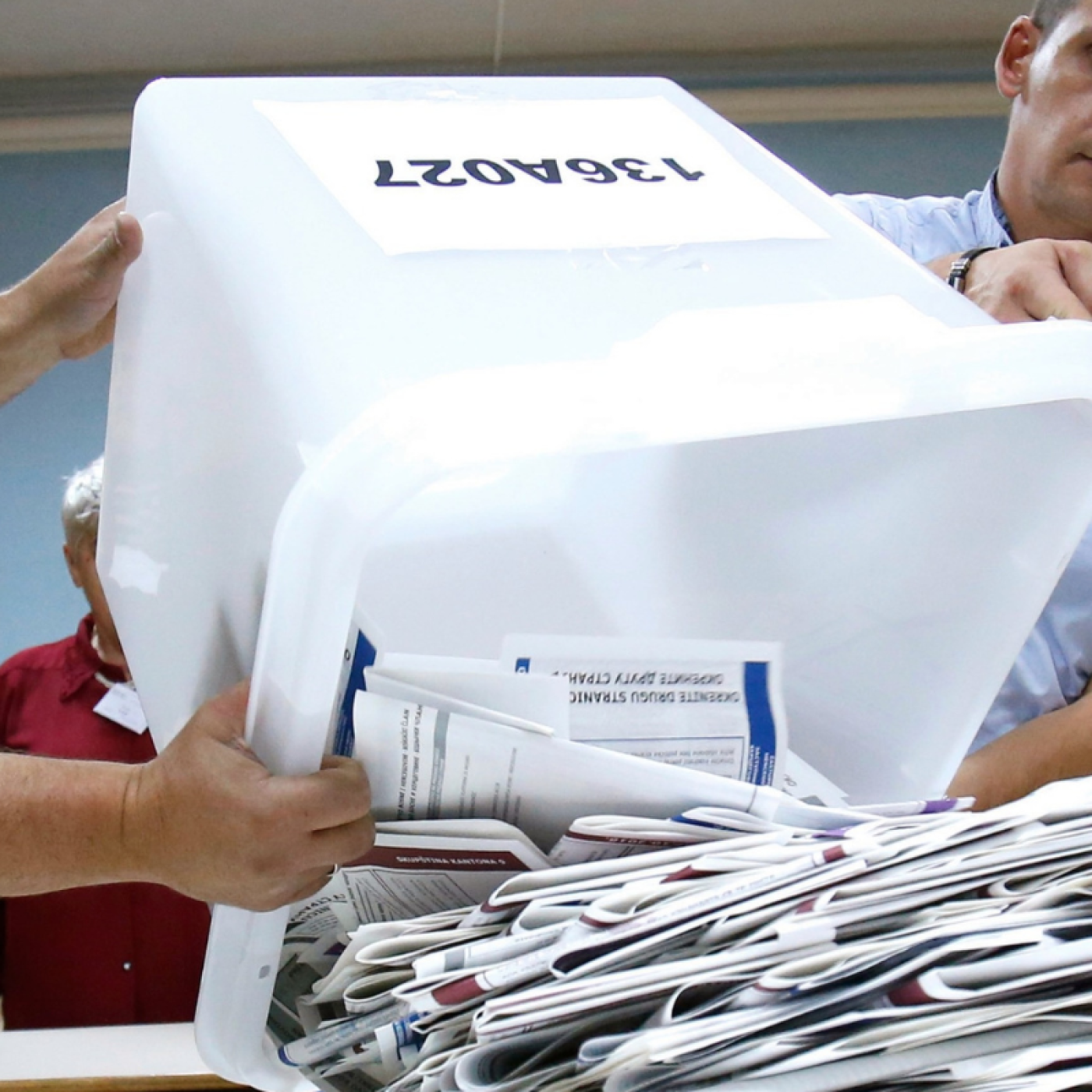 Three Bosnian election workers empty paper ballots from a container onto a table.