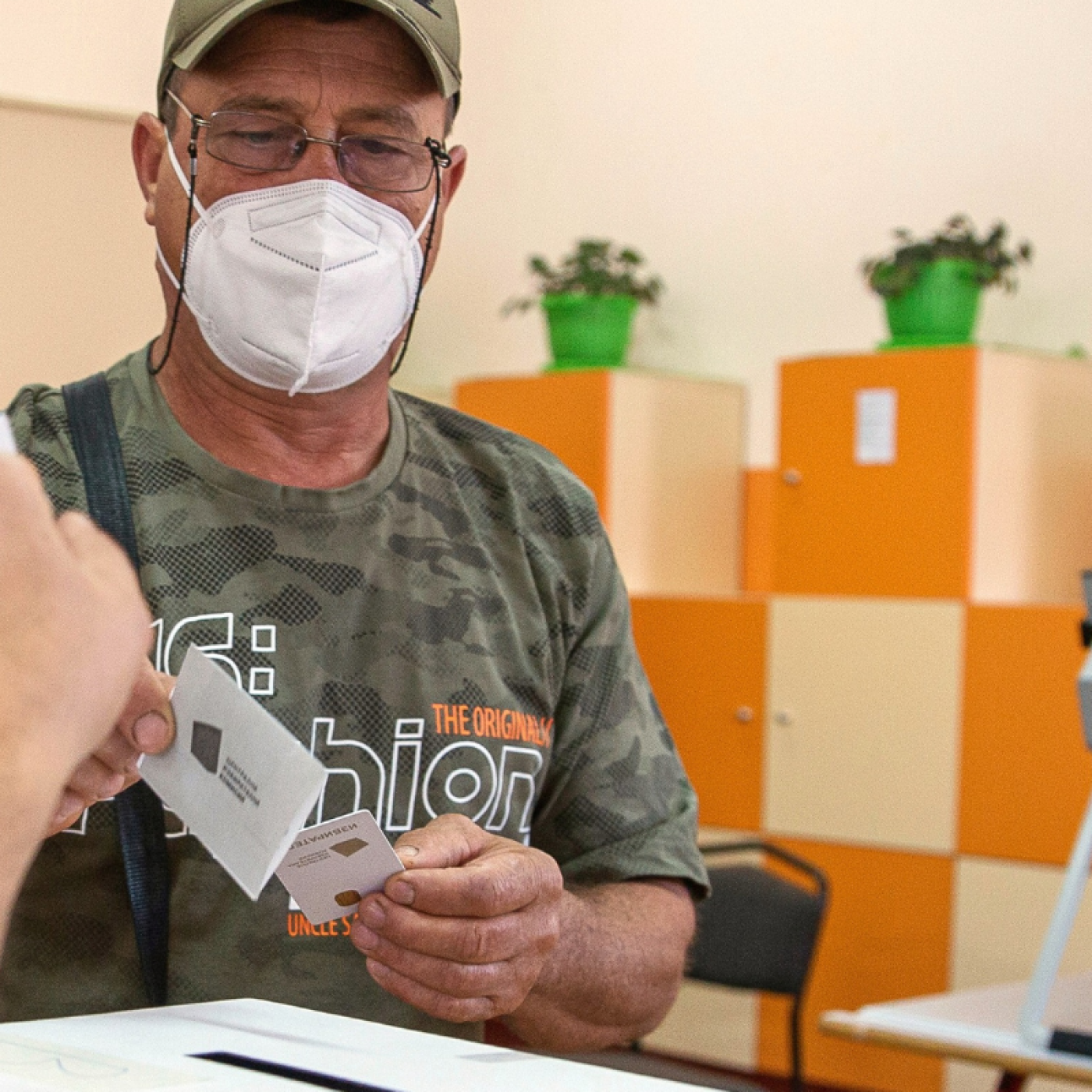 A man wearing a face mask casts his vote into a white ballot box inside a polling station.