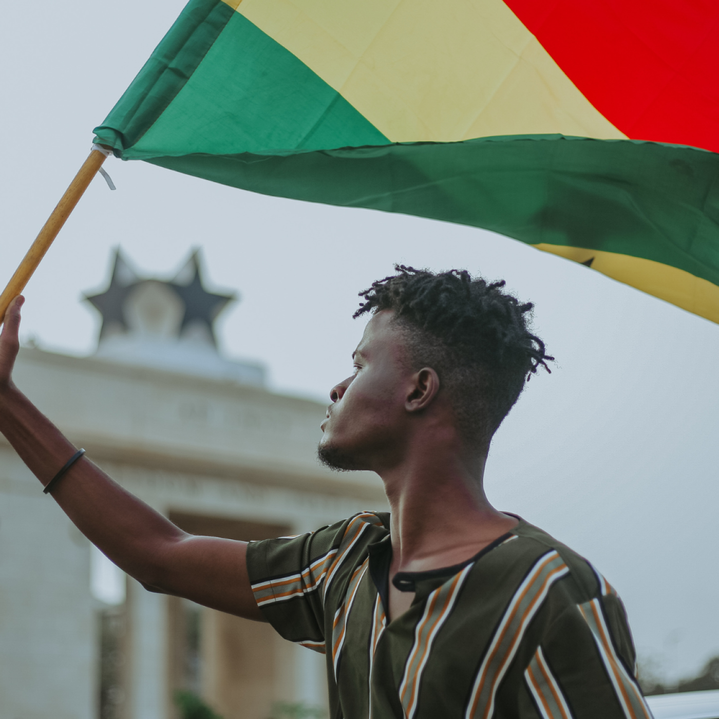 Young man stands on city street in Ghana with Ghanian flag