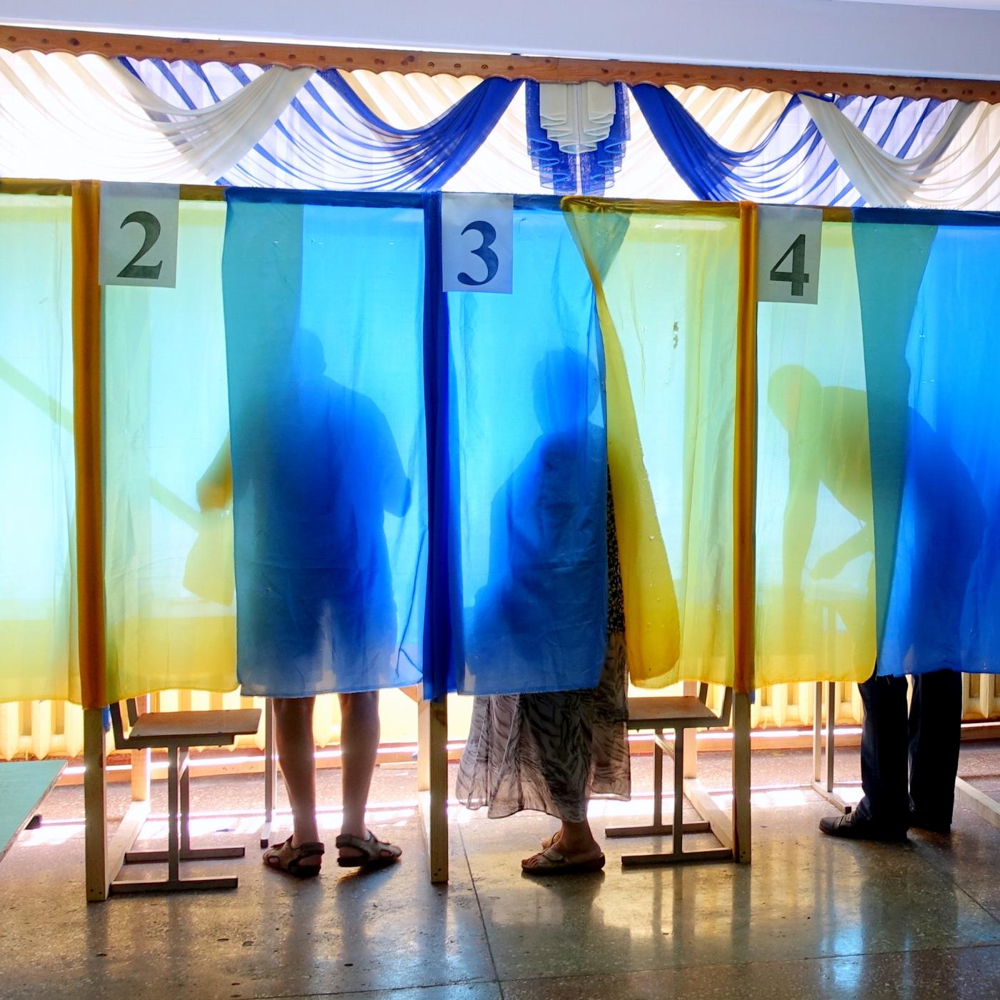 Voters stand behind blue and yellow curtains in poll booths.