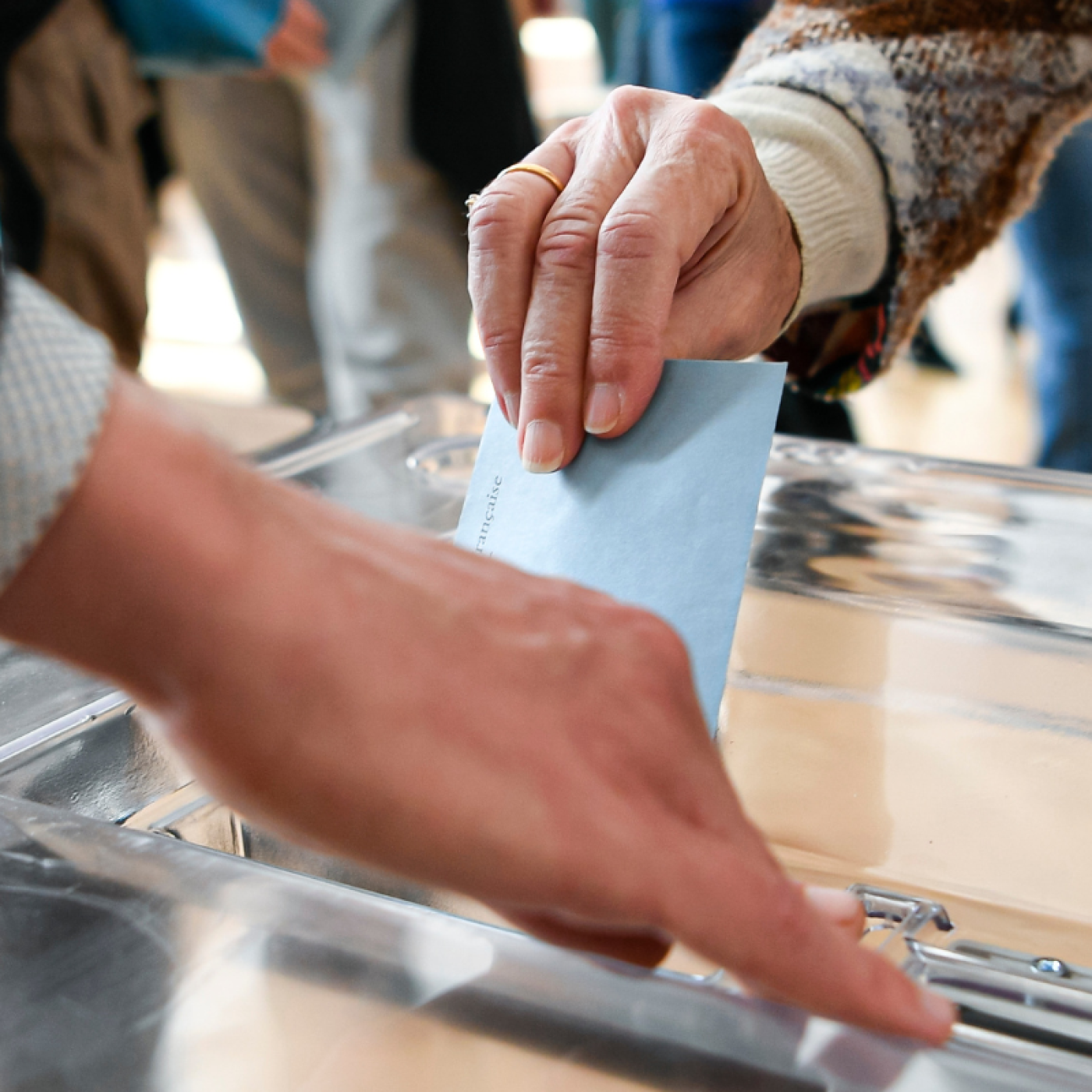 picture shows a person voting with a ballot paper in its envelope just before being placed in the ballot box