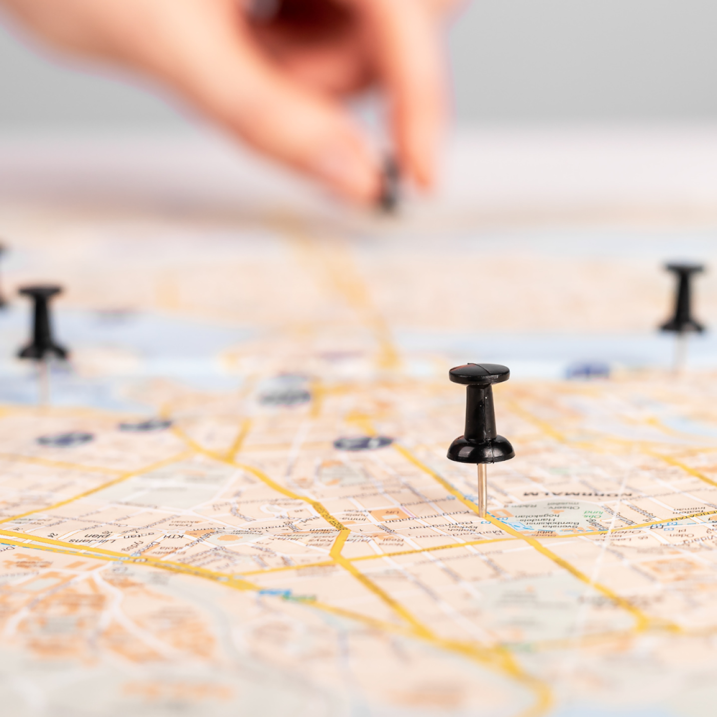 Roadmap with pushpins spread out. Hand in the background with additional pushpin.
