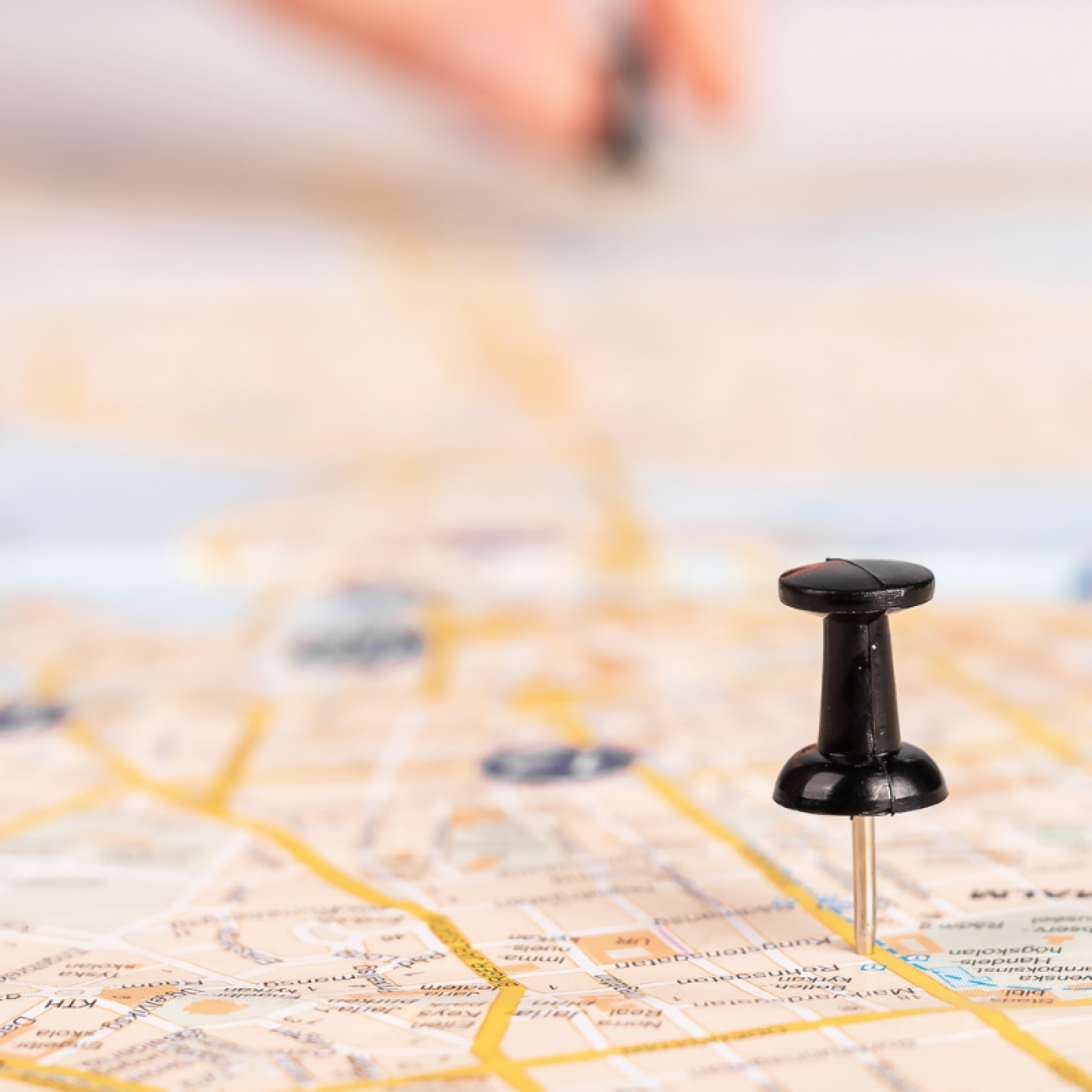 Push pins laid out on a road map. hand in the background with additional pin.