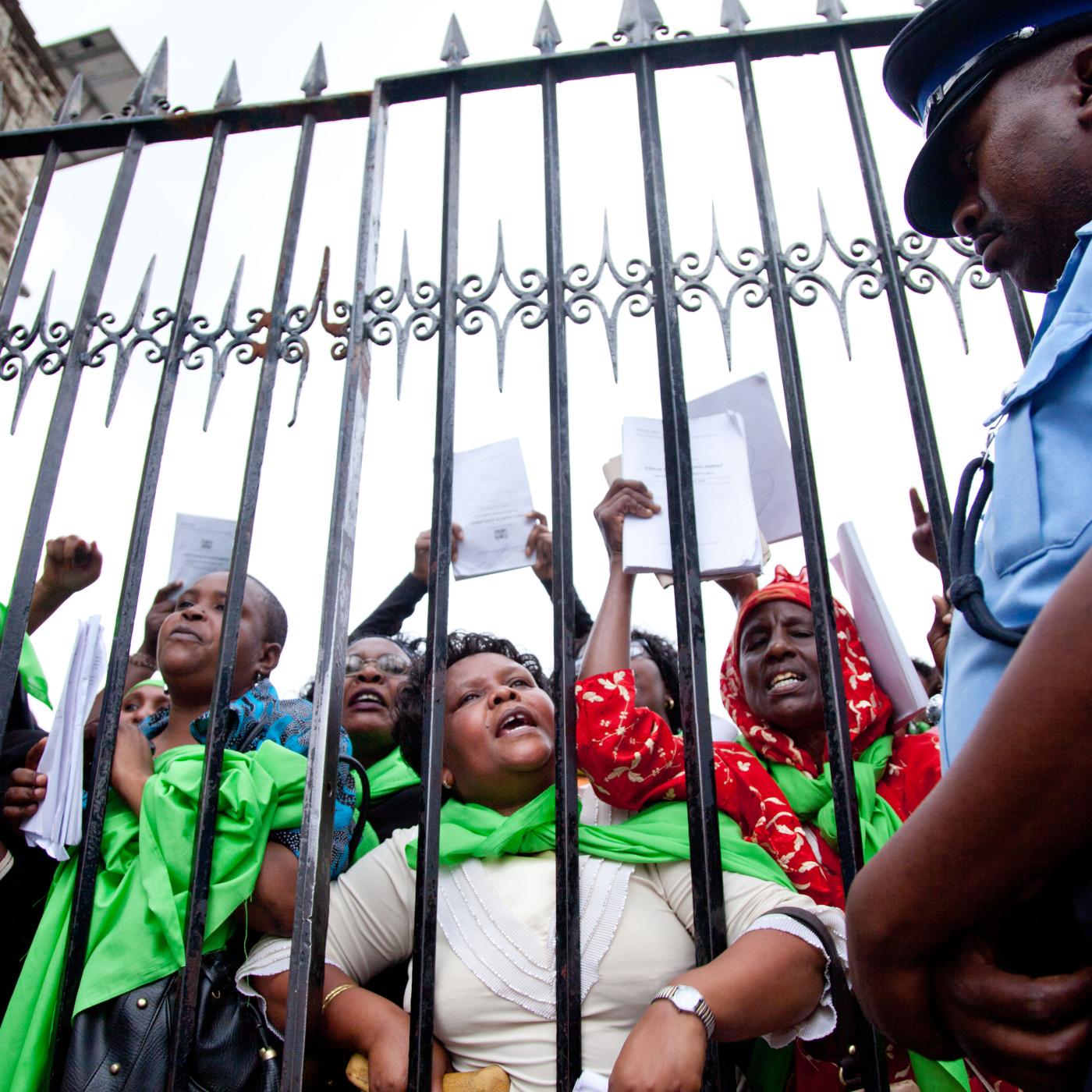 An iron fence separates a police officer and a crowd of protesting women.