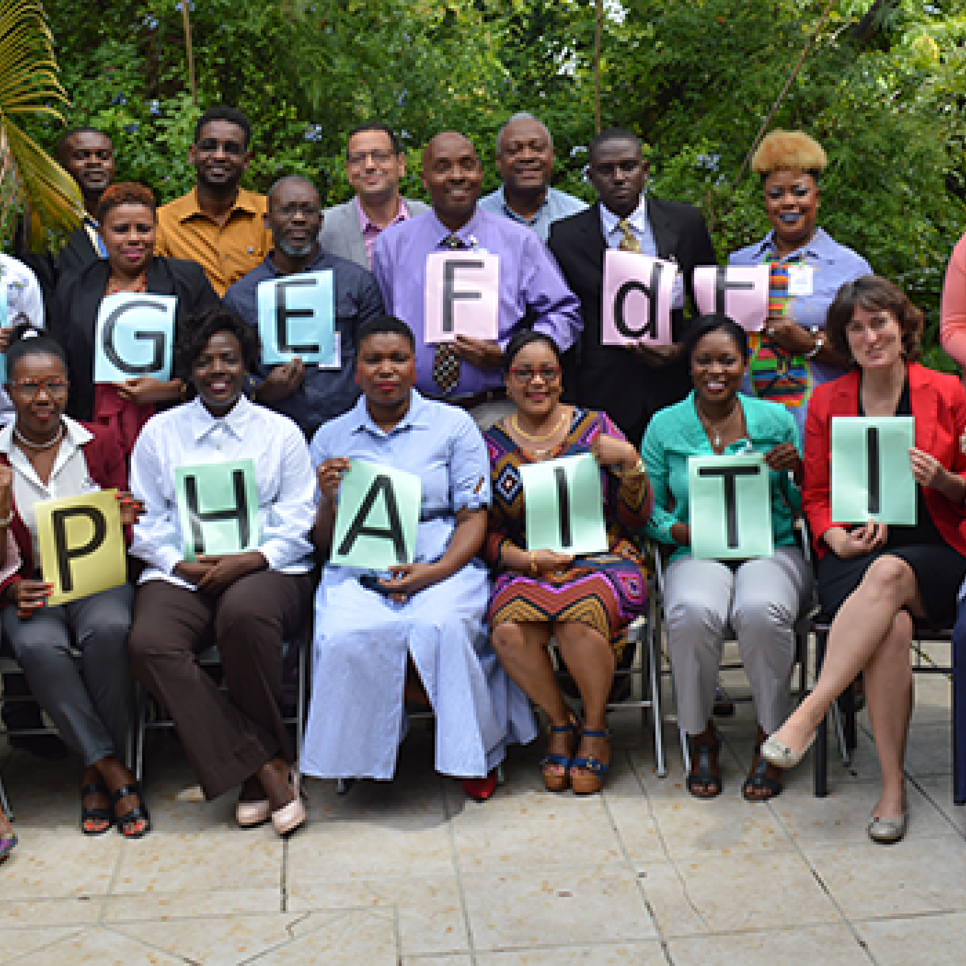 Participants and facilitators from the TtF workshop hold up signs that spell out, "BRIDGE FdF 2019 CEP Haiti USAID" 